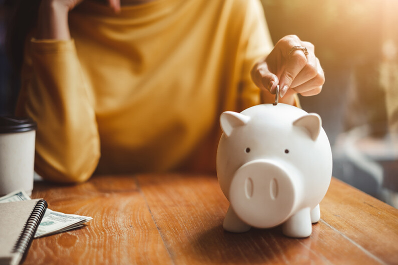 Women placing money into a white piggy bank